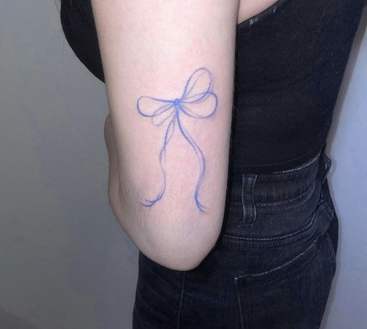 a woman's arm with a bow tattoo on the left side of her arm