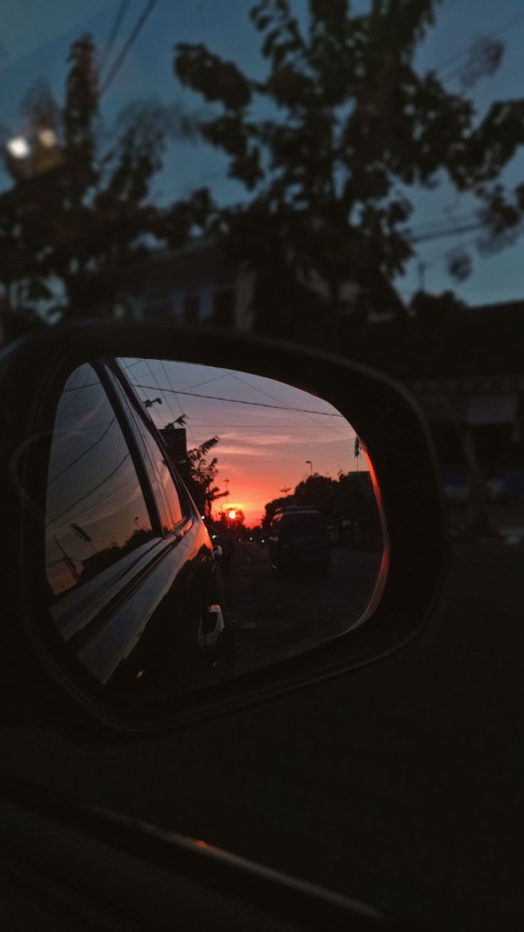 the sun is setting in the rear view mirror