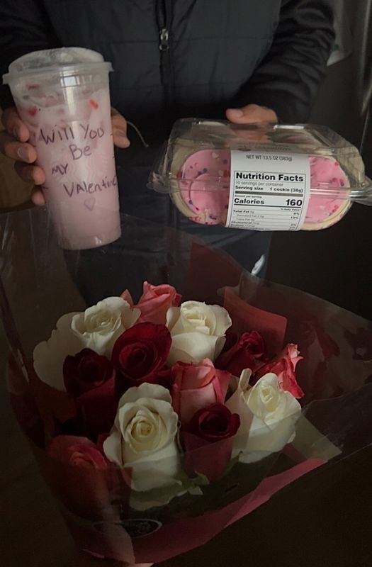 a person holding a pink and white cup next to a bouquet of red and white roses