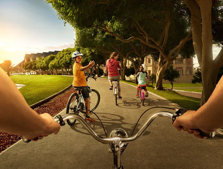 two people riding bikes on a paved path with trees and grass in the back ground