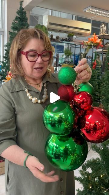 a woman is holding christmas ornaments in front of a christmas tree and talking to the camera