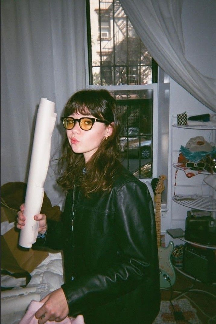 a woman wearing glasses holding a large roll of paper in her hand and looking at the camera