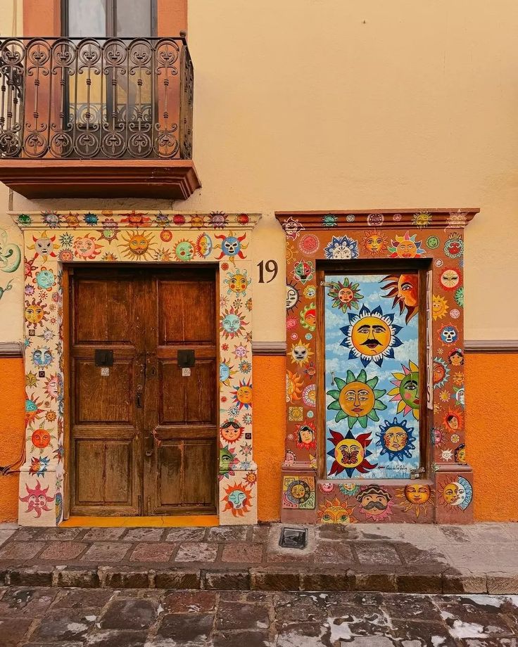 two wooden doors are in front of an orange building with floral designs on the walls