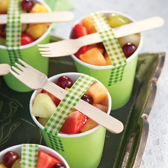 small cups filled with different types of fruit and wooden utensils on a tray