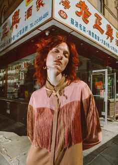 a woman with red hair standing in front of a chinese store wearing a brown shirt and tie