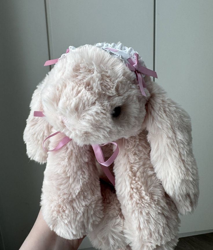 a white stuffed animal with pink ribbon around it's neck and legs, sitting on top of a person's leg