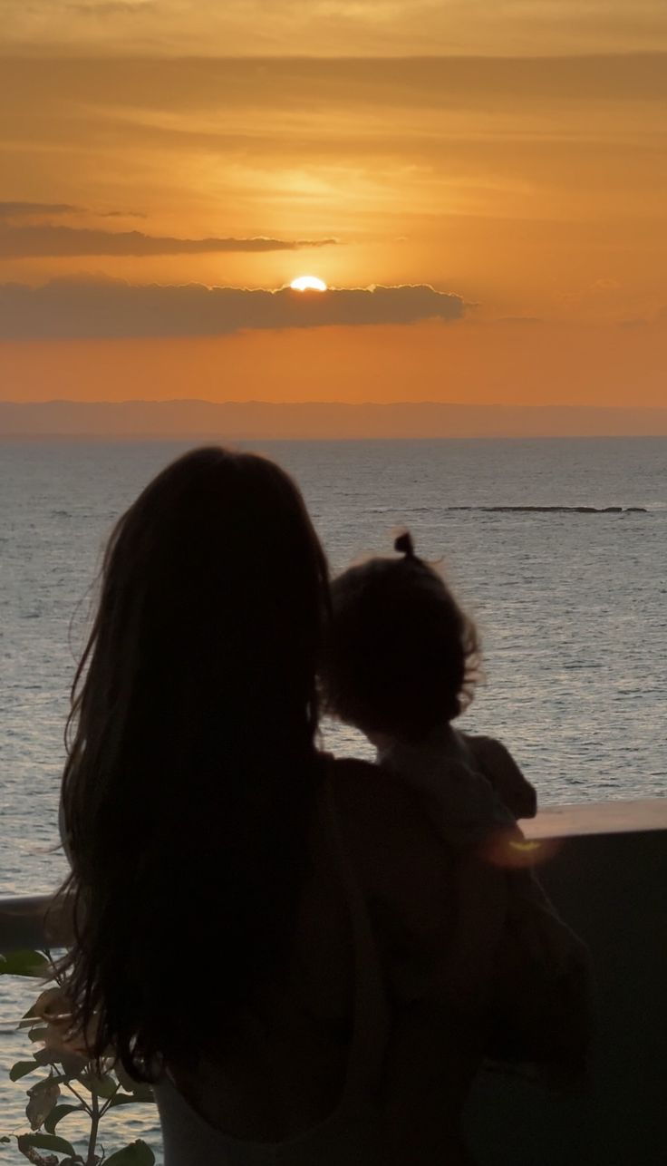 a woman holding a baby looking out at the ocean