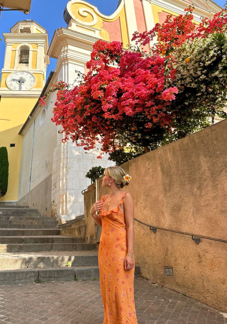 a woman in an orange dress is standing outside