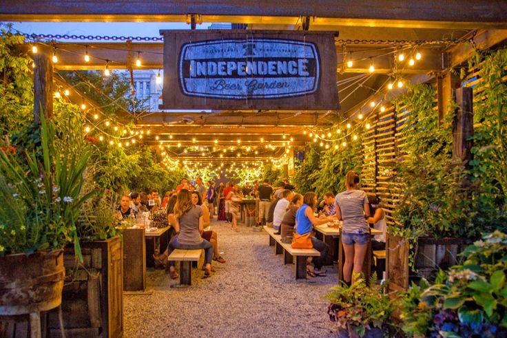 people are sitting at tables under lights in an outdoor restaurant with potted plants on either side