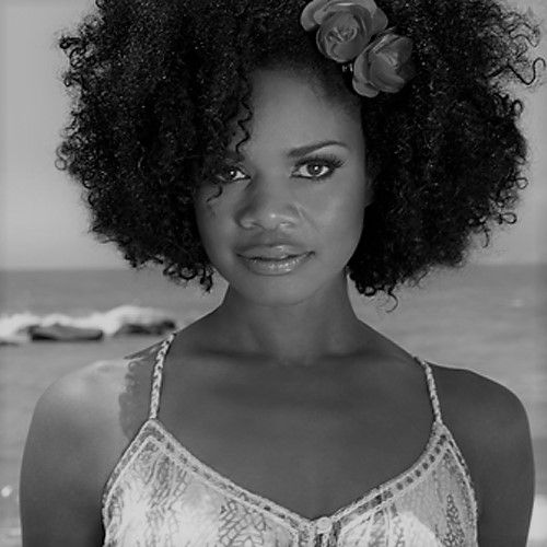 a black and white photo of a woman with curly hair wearing a tank top by the ocean