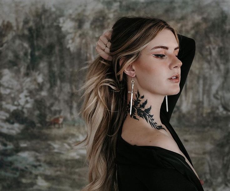 a woman with long hair and piercings on her neck stands in front of a wall