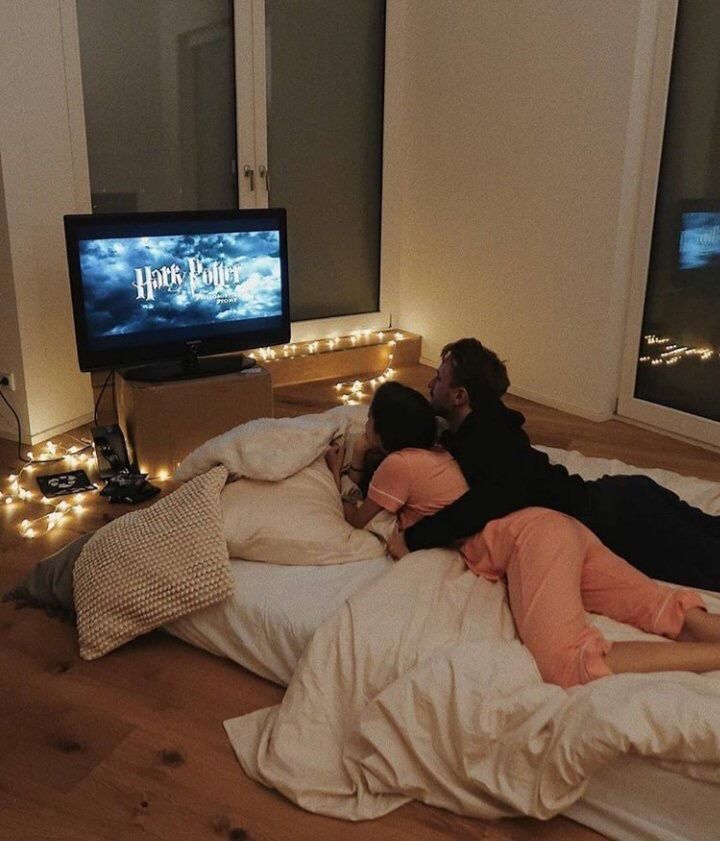 two people laying on a bed in front of a tv