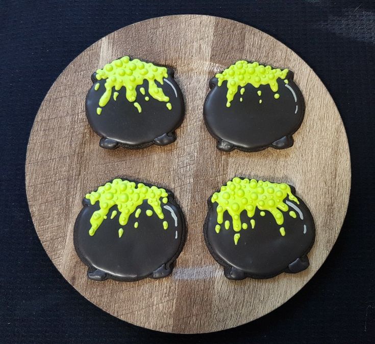 four decorated cookies sitting on top of a wooden plate with black icing and yellow sprinkles