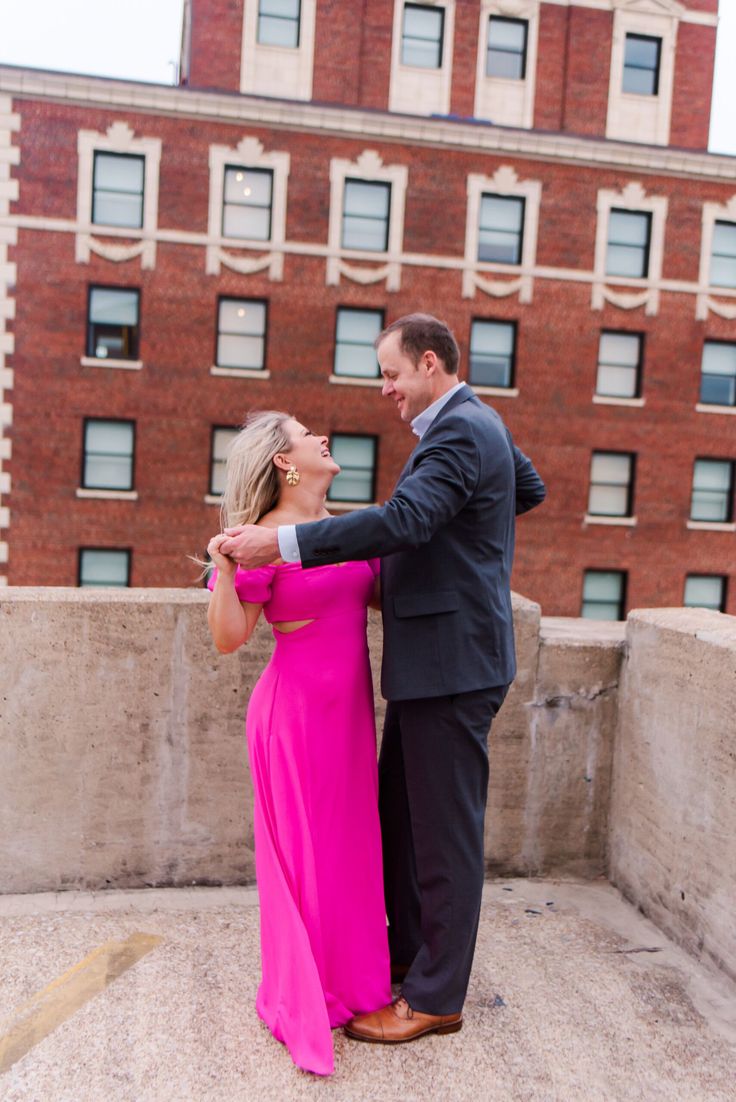 a man in a suit and woman in a pink dress standing on a roof with their arms around each other