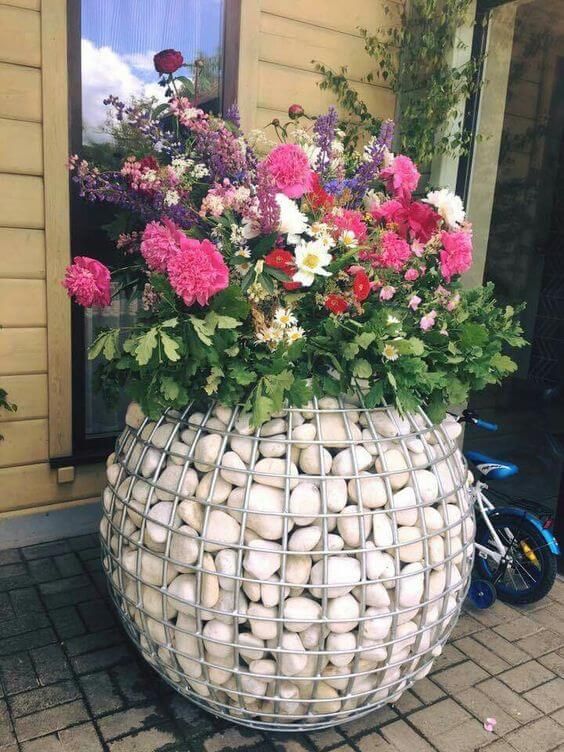 a vase filled with lots of flowers sitting on top of a brick floor next to a window