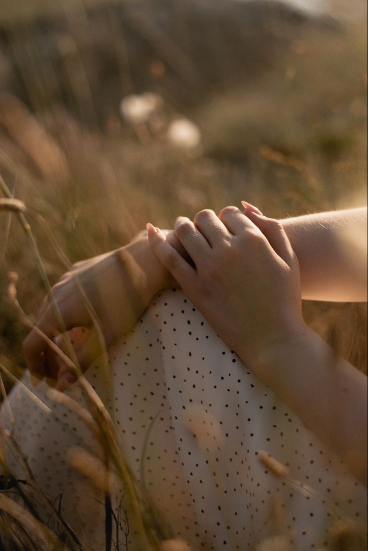 a woman in a white dress is holding her hand over her shoulder while sitting in tall grass