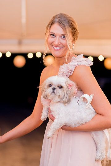 a woman in a pink dress holding a white dog on her arm and smiling at the camera