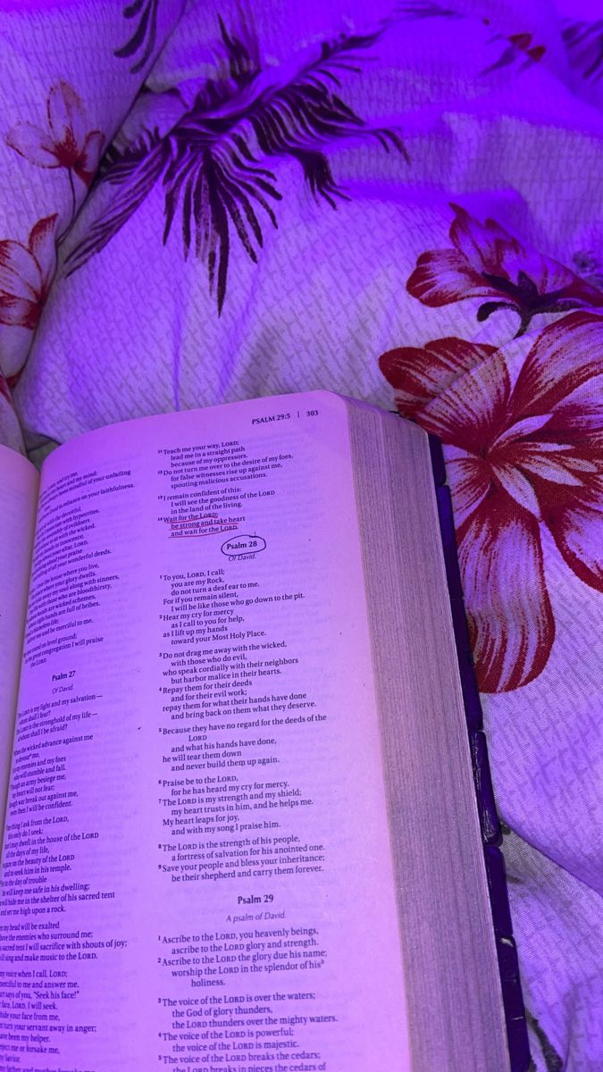 an open book sitting on top of a bed next to a purple flowered comforter