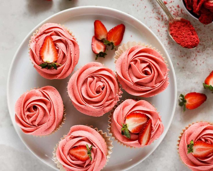 cupcakes with pink frosting and strawberries on a white plate next to some strawberries