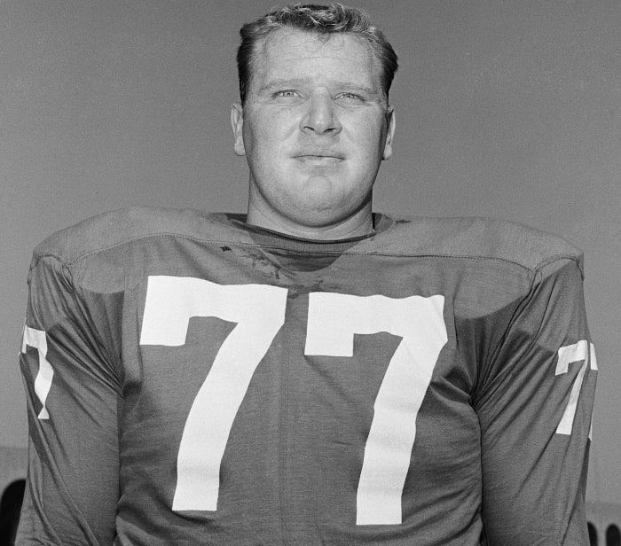 a black and white photo of a man wearing a football uniform with the number 77 on it