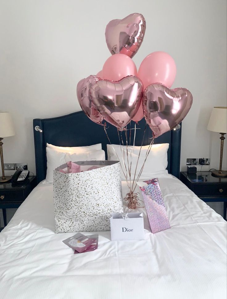 a bed with pink and silver heart balloons on top of it next to a pillow