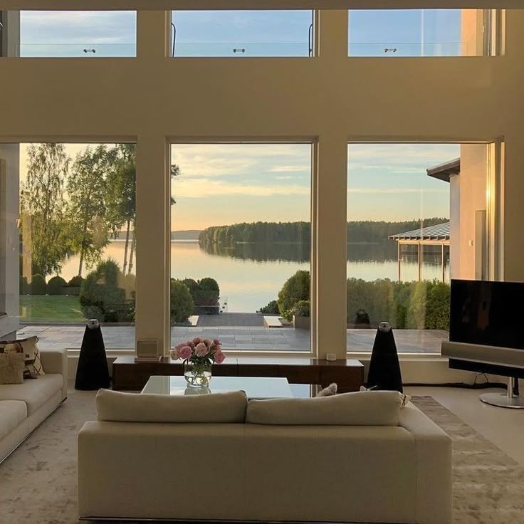 a living room filled with furniture and large windows looking out onto the water at sunset