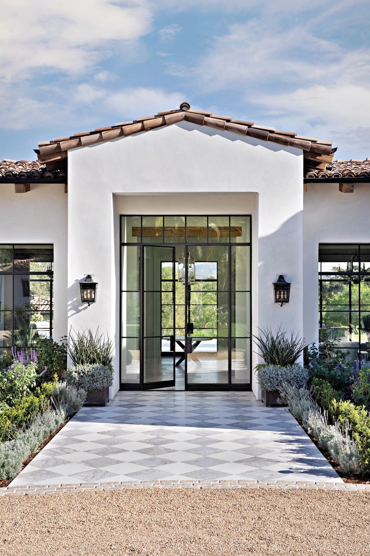 the front entrance to a white house with glass doors and plants in pots on either side