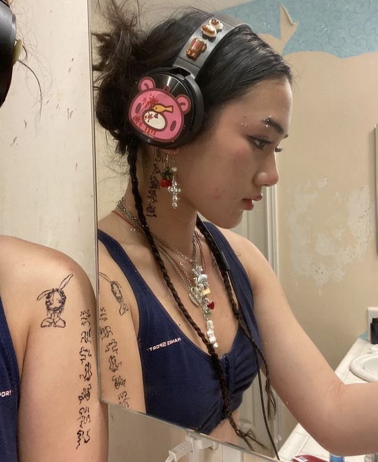 a woman with headphones is looking at her cell phone in the mirror while she has tattoos on her arm