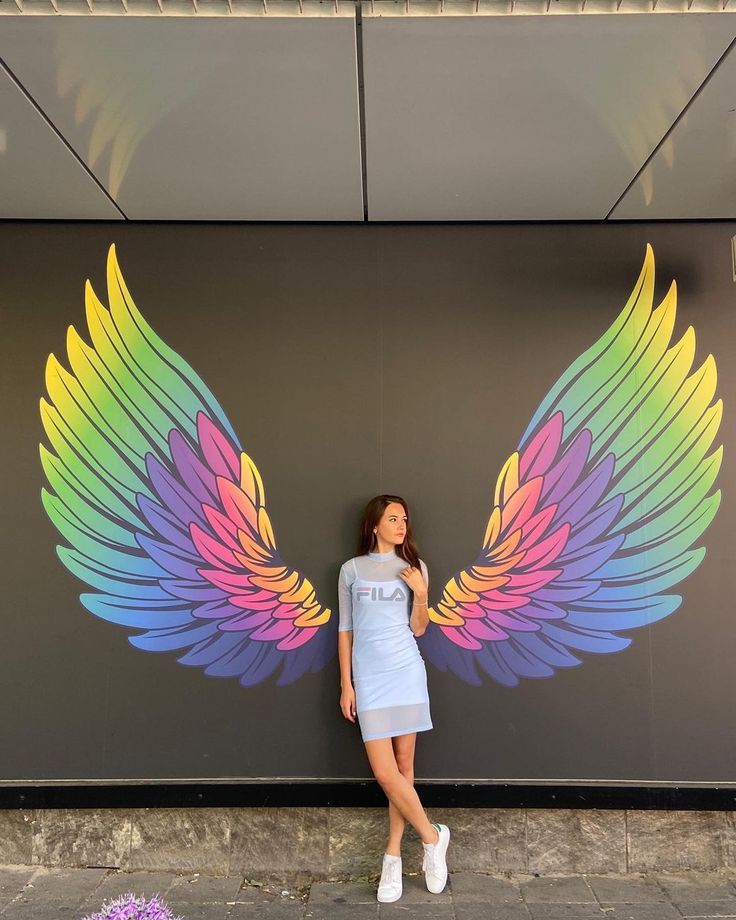 a woman standing in front of a wall with wings painted on it's side