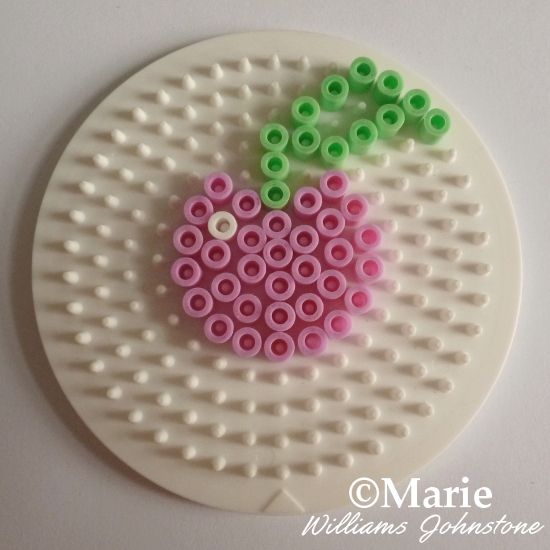 a piece of art made out of plastic beads on top of a white plate with green and pink circles