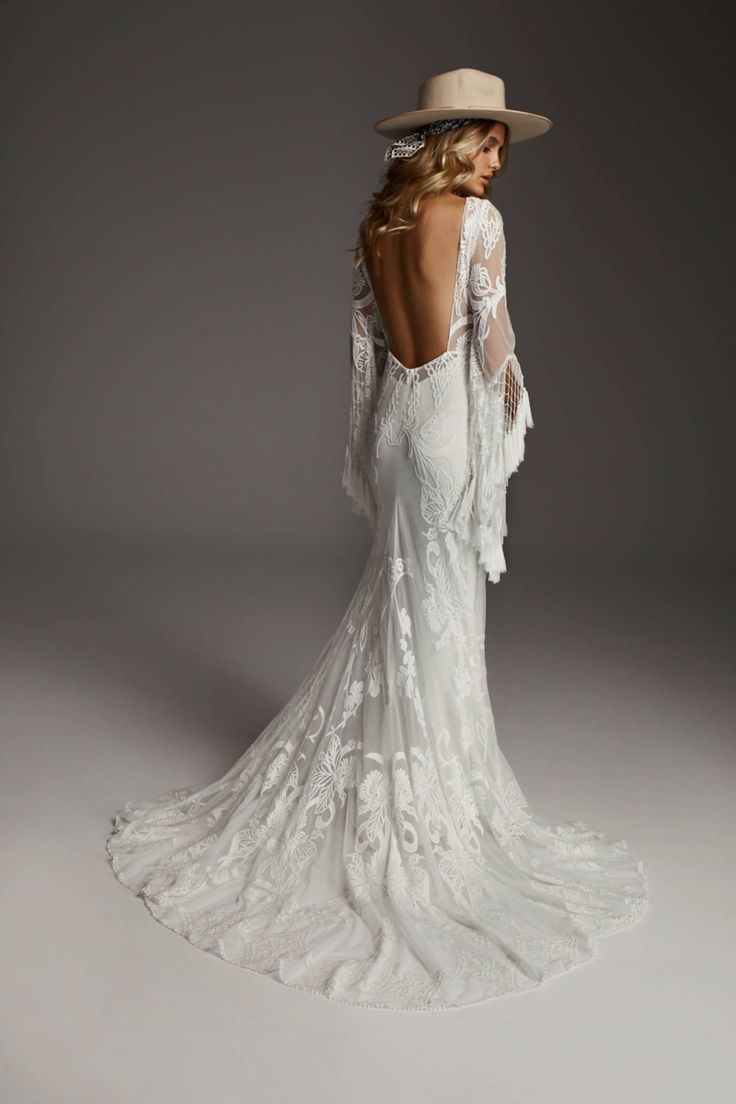 the back of a woman wearing a white wedding dress with long sleeves and an open back