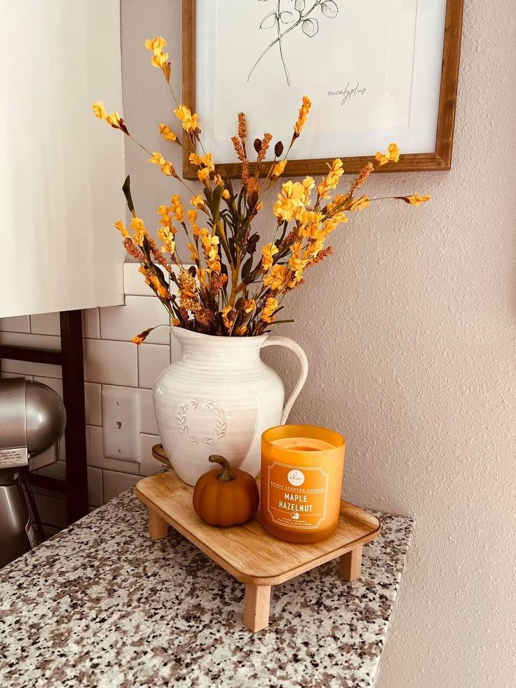 a white vase filled with yellow flowers sitting on top of a counter next to a candle