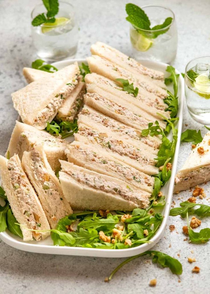 a white plate topped with cut up sandwiches next to glasses of water and minty garnish