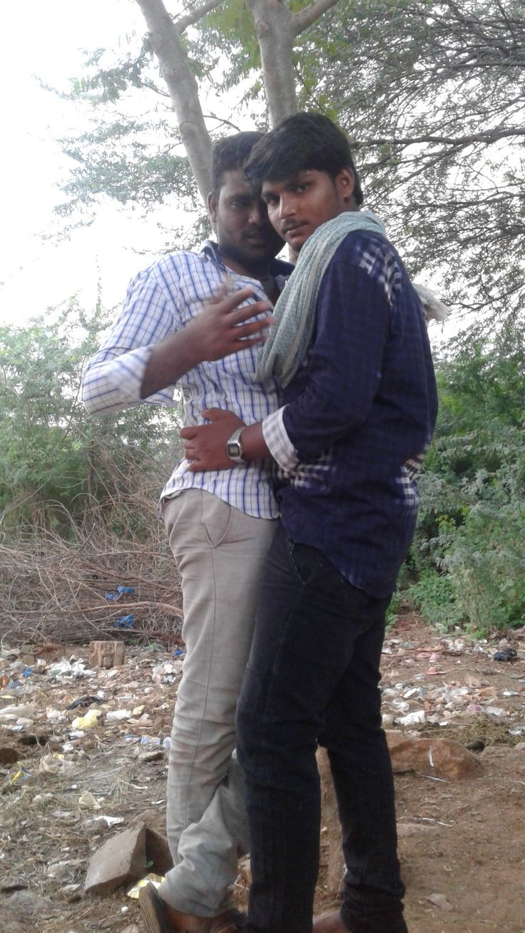 two men standing next to each other in front of trees and trash on the ground