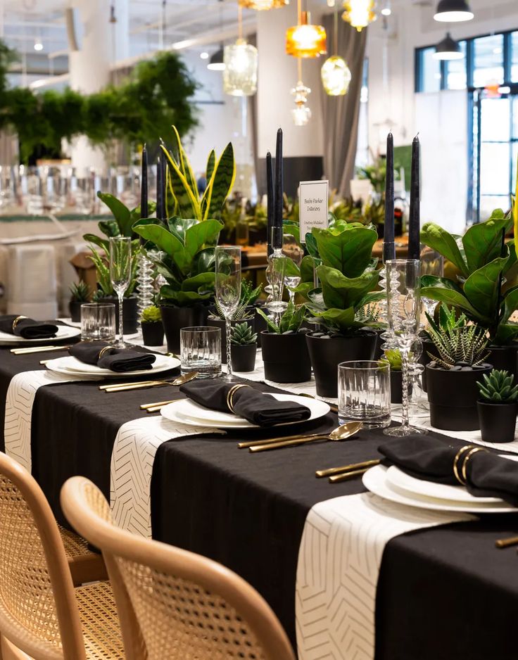 a table set with black and white place settings, plants in vases on the tables