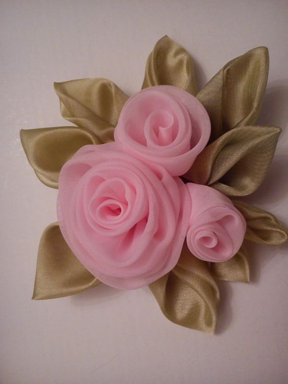 three pink flowers with green leaves on a white surface and gold ribbon around the edges