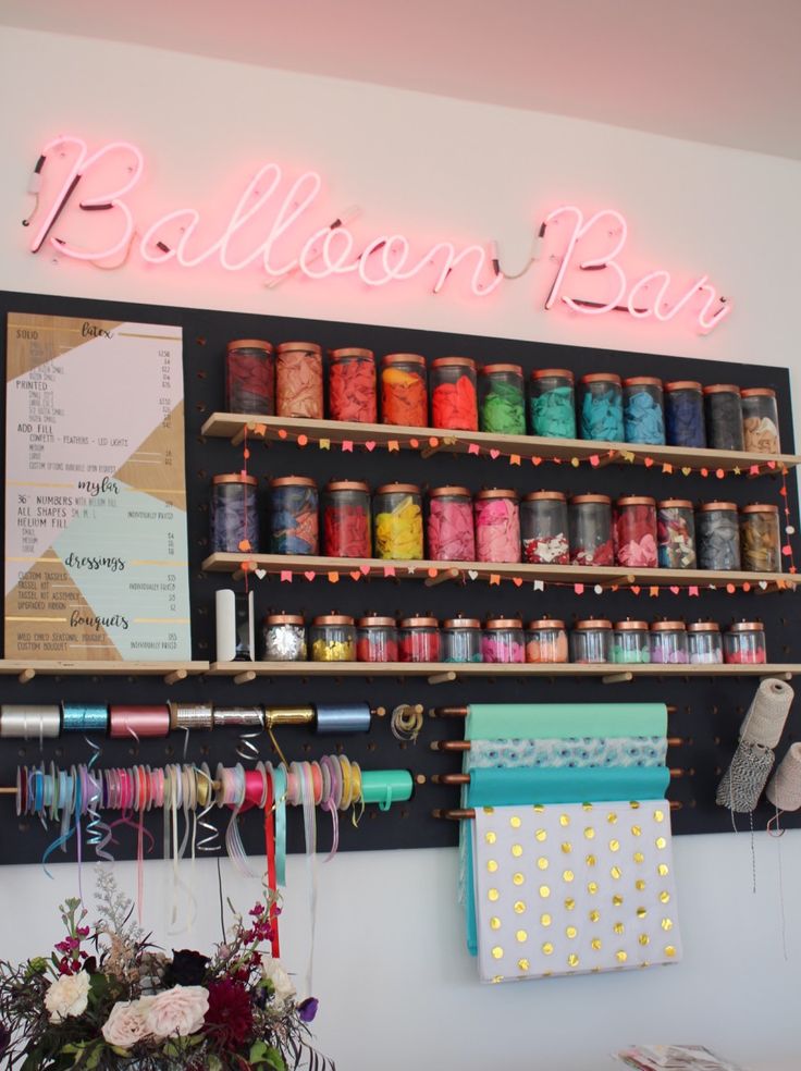 there is a neon sign that says balloon bar on the wall next to some spools of thread