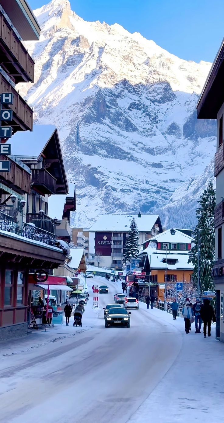 cars parked on the side of a road in front of snow covered mountains and buildings