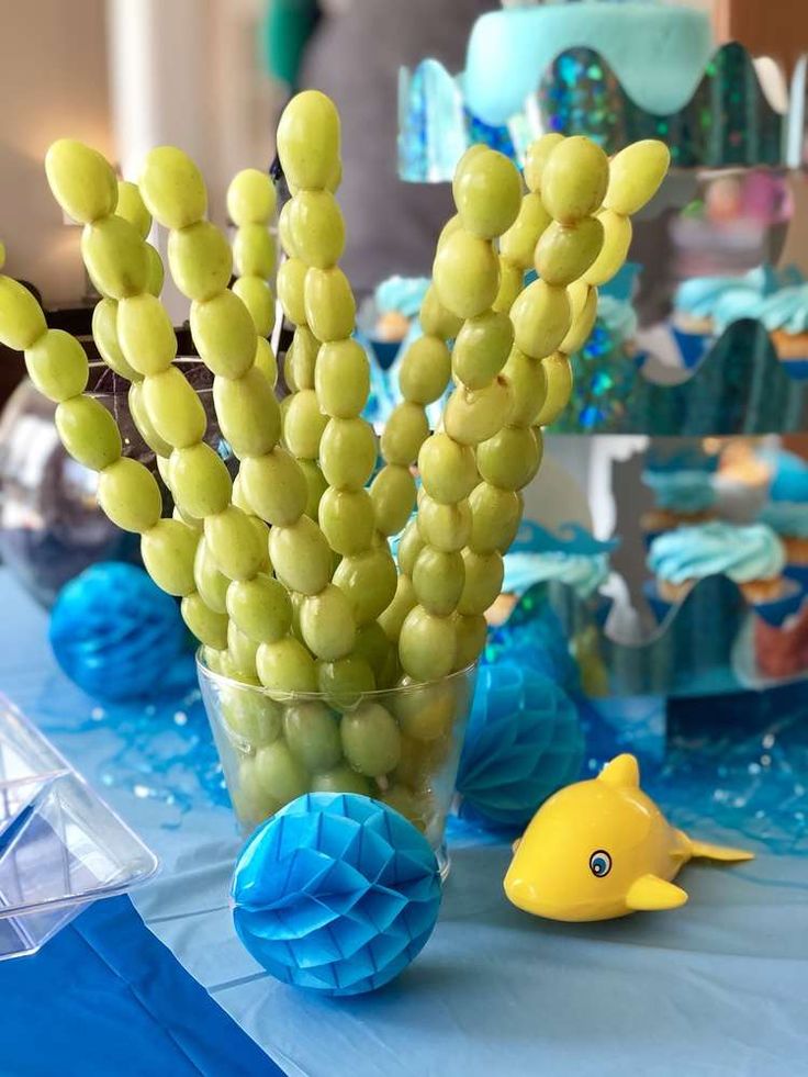 a table topped with a vase filled with yellow and green fruit next to a fish