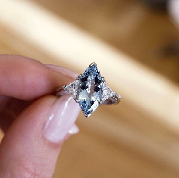 a woman's hand holding an engagement ring with a blue diamond in the center