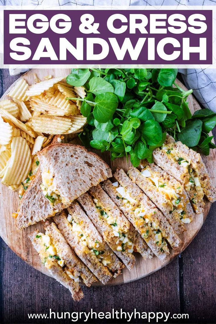 an egg and cheese sandwich on a wooden plate with potato chips, lettuce and spinach