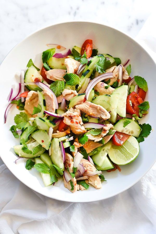 a white bowl filled with cucumber, chicken and red onion salad on top of a table