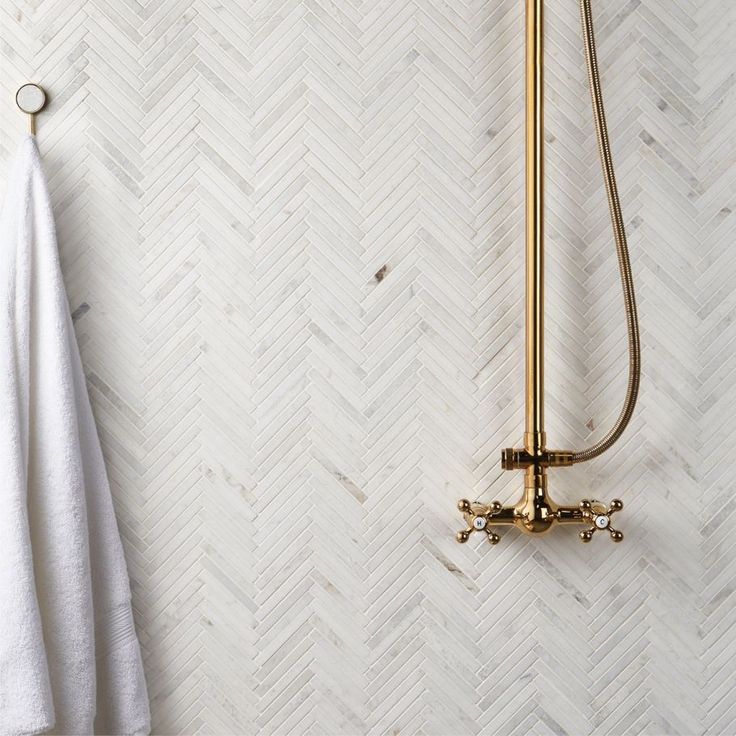 a white towel hanging next to a gold shower faucet in a bathroom with herringbone wallpaper