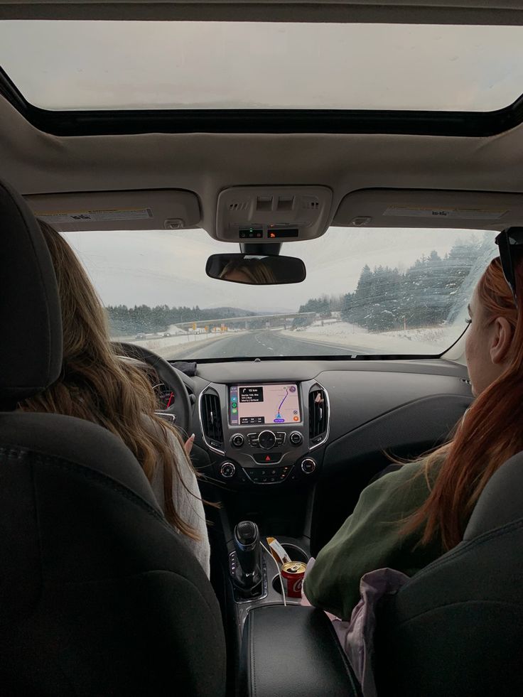 two women sitting in the back seat of a car looking at something on the screen