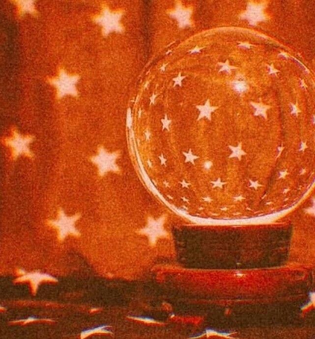 a glass ball with stars on it sitting on top of a wooden table next to a curtain