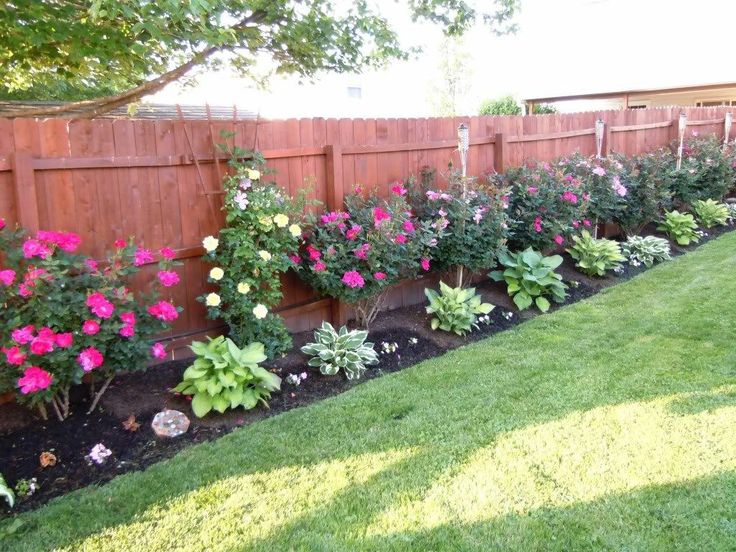 a garden filled with lots of colorful flowers next to a wooden fence and green grass