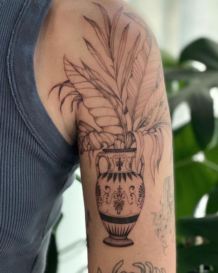 a woman's arm with a potted plant and leaves tattoo on her left arm