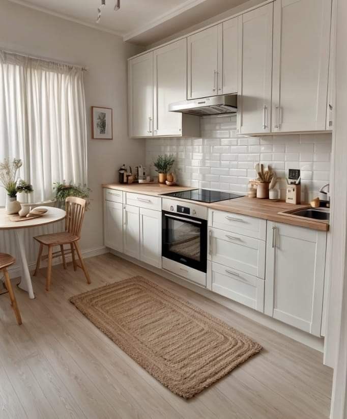 a kitchen with white cabinets and wooden flooring next to a dining room table in front of a window