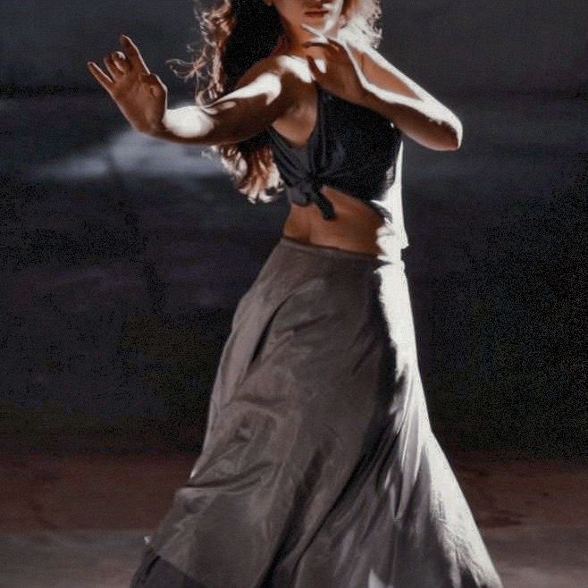 a woman in a long skirt is dancing with her hands out to the side,