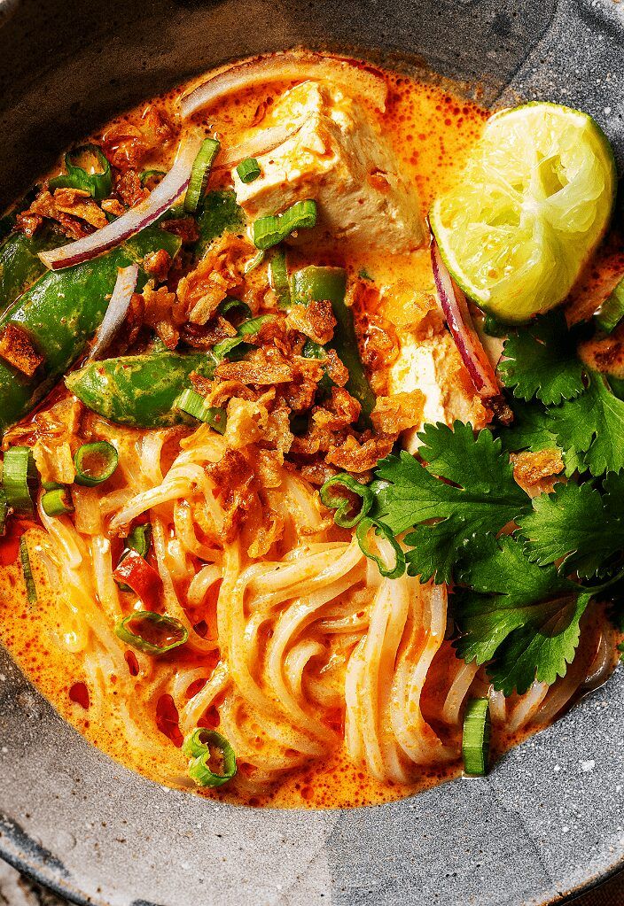 a bowl filled with noodles, meat and vegetables next to a lime wedge on the side